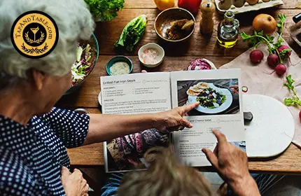Person reviewing a standardized recipe book while preparing ingredients on a kitchen table